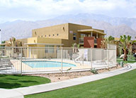 Outdoor amenity area with landscaping and a pool surrounded by decorative fencing. One- and two-story stucco buildings are in the background.